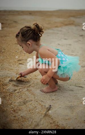 Niedliches Kleinkind, das in blauem Badeanzug im Sand spielt Stockfoto