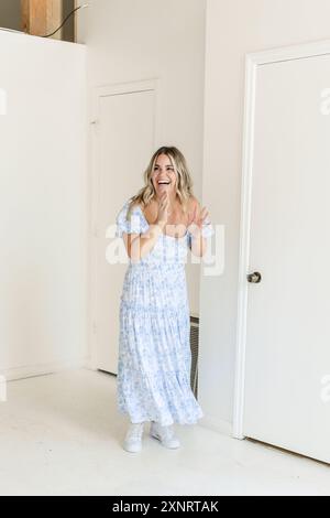 Frau in blauem Kleid, lachend und drinnen stehend, mit Turnschuhen Stockfoto