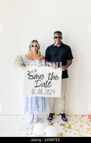Ein Paar hält ein Schild mit dem Namen „Save the Date“ und dem Hochzeitsdatum Stockfoto