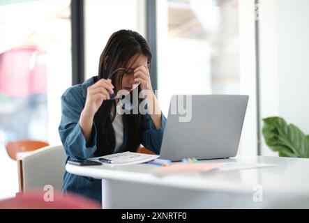 Eine Frau sitzt an einem Schreibtisch mit einem Laptop und einem Stapel Papiere Stockfoto