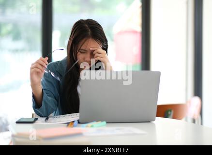 Eine Frau sitzt an einem Tisch mit einem Laptop und einem Stapel Papiere Stockfoto