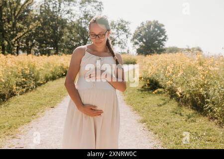 Schwangere Frau im Leinenkleid auf dem Weg mit Wildblumen Stockfoto