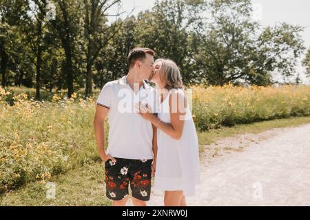 Ein junges Paar küsst sich auf einem Weg mit Wildblumen und Bäumen Stockfoto