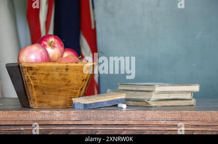 Eine Schüssel Äpfel auf dem Schreibtisch eines Lehrers mit Kreide, Radiergummi und Büchern Stockfoto