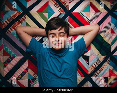 Entspannter Teenager, der auf einer farbenfrohen Decke liegt, die von oben aufgenommen wurde. Stockfoto