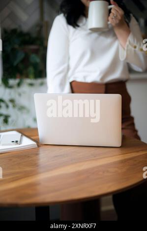 Frau, die Kaffee trinkt, Laptop auf einem Holztisch, Inneneinrichtung. Stockfoto