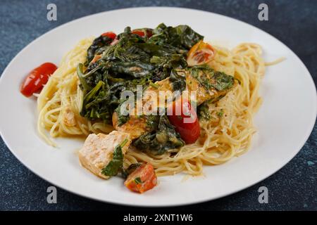 Lachsfilet in cremiger Sauce mit Spaghetti, Frischkäse und Spinat und Kirschtomaten in Nahaufnahme auf dem Teller Stockfoto