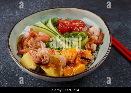 Frisches Meeresfrüchte-Rezept. Shrimps Poke Bowl mit Reis, grünen Zwiebeln, Tomaten, Avocado, Mango. Food Concept Poke Schüssel auf grauem Hintergrund Stockfoto