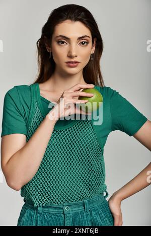 Eine junge Frau im grünen Outfit hält Apfel, ihr Ausdruck fesselnd. Stockfoto