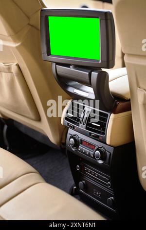 Innenraum in cremefarbenen Ledertönen von luxuriösem, modernem Auto. Schwenkbares grünes isoliertes Display für Beifahrer auf den Rücksitzen mit Medienbedienfeld Stockfoto