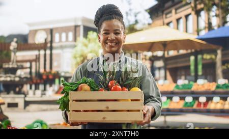 Porträt einer multiethnischen Frau mittleren Alters, die einen Straßenverkäufer mit frischen ökologischen Agrarprodukten verwaltet. Fröhlicher, stylischer afrikanischer Farmer schaut in die Kamera und lächelt charmant Stockfoto