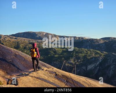 Ein einsamer Wanderer steht auf einer glitzernden Felsenoberfläche und bestaunt die atemberaubende norwegische Landschaft, die von der Morgensonne beleuchtet wird. Lysefjord Kjeragbolten Kjerag Norwegen Stockfoto