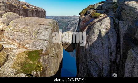 Ein atemberaubender Blick auf einen prekären Felsen, der sich über ruhigen Gewässern vor Norwegens dramatischen Klippen und dem pulsierenden Himmel balanciert. Kjerag Kjeragbolten Lysefjord Norwegen Stockfoto