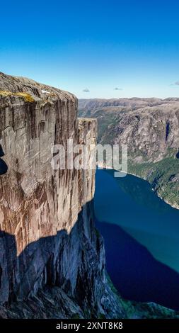 Atemberaubende Klippen erheben sich dramatisch über einem tiefblauen Fjord, umgeben von üppigen grünen Bergen unter hellem Himmel. Kjerag Kjeragbolten Lysefjord Norwegen Stockfoto