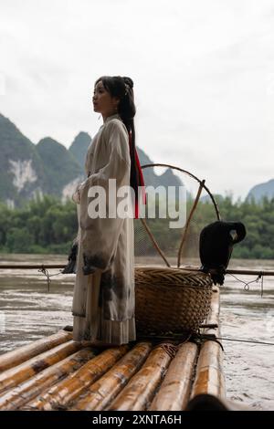 Chinesisches Hanfu-Mädchen, das ihre Haare repariert, während es auf einem Bambusfloß am Fluss Li, Xingping, steht Stockfoto