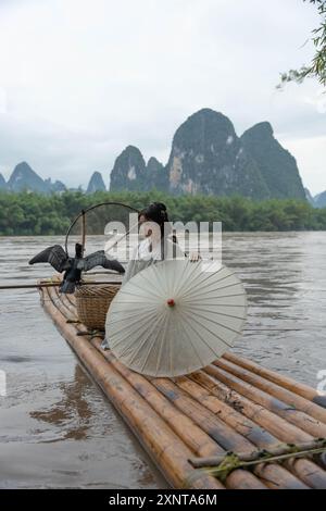 Hanfu-Mädchen mit Schirm auf Bambusfloß in Xingping posiert mit Kormoranen Stockfoto