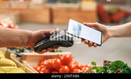 Verbraucher, die Agrarerzeugnisse aus ökologischem Anbau mit einer digitalen Kreditkarte kaufen, um mit einer Smartphone-Software über die kontaktlose Online-NFC-Technologie an einem Point-of-Sale-Terminal der Bank zu bezahlen Stockfoto