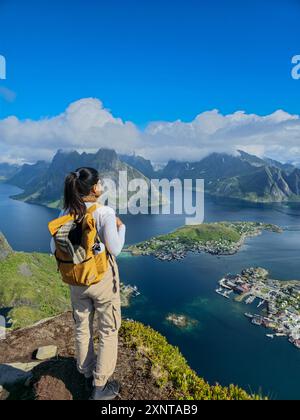 Ein Wanderer bewundert die atemberaubenden Ausblicke auf die Lofoten-Inseln, umgeben von dramatischen Bergen und glitzerndem Wasser unter einem klaren blauen Himmel. Stockfoto