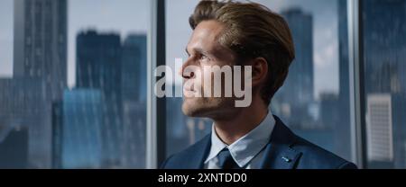 Porträt eines erfolgreichen kaukasischen Geschäftsmannes in einem maßgeschneiderten Anzug, der im Büro steht und aus dem Fenster auf Big City mit Wolkenkratzern blickt. Investitionsmanager Projektstrategie Planen. Stockfoto