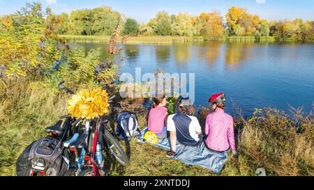 Familie auf Fahrrädern Herbst Radfahren im Freien, aktive Eltern und Kind auf Fahrrädern, aus der Vogelperspektive auf glückliche Familie mit Kind, die sich in der Nähe des wunderschönen Flusses entspannt Stockfoto