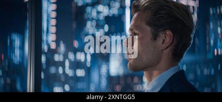 Nahaufnahme Porträt eines gutaussehenden kaukasischen Geschäftsmannes in einem Anzug, der neben dem Fenster im Großstadtbüro mit Wolkenkratzern in der späten Nacht steht. Männlicher CEO, der nachdenklich aus dem Fenster schaut Stockfoto