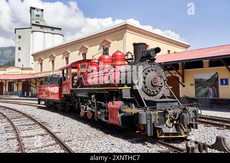 Eine klassische rote Dampflokomotive steht an einem klaren Tag an einem historischen Bahnhof und zeigt alte Transportmittel. Stockfoto