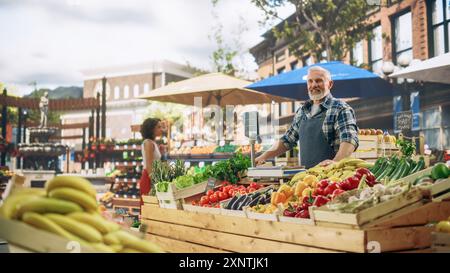 Cheerful Street Vendor, der einen kleinen Bauernmarkt betreibt und nachhaltiges Obst und Gemüse verkauft. Glücklicher Mann mittleren Alters, der morgens auf Gäste wartet Stockfoto
