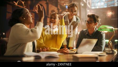 Verschiedene Gruppe von Studenten, die an einem Projekt in einer modernen Bibliothek zusammenarbeiten. Junge Erwachsene, die sich mit Diskussionen beschäftigen, Laptop für Forschung und E-Learning nutzen, freudige akademische Interaktion erleben Stockfoto