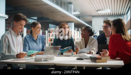 Verschiedene Gruppe von Studenten, die an einem Projekt in einer modernen Bibliothek zusammenarbeiten. Junge Männer und Frauen, die Laptops und Bücher verwenden, an Gruppendiskussionen teilnehmen und gemeinsam lernen. Stockfoto