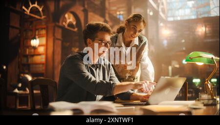 Studentinnen und Studentinnen studieren in einer Universitätsbibliothek. Frau, die ihrem Klassenkameraden mit Hausaufgaben auf einem Laptop hilft. Paare verwenden Laptop Computer für ein Gruppenforschungsprojekt Stockfoto