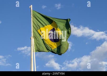 Goiania, Goias, Brasilien – 2. August 2024: Die brasilianische Flagge flattert auf dem Fahnenmast mit dem Himmel und einigen Wolken im Hintergrund. Stockfoto