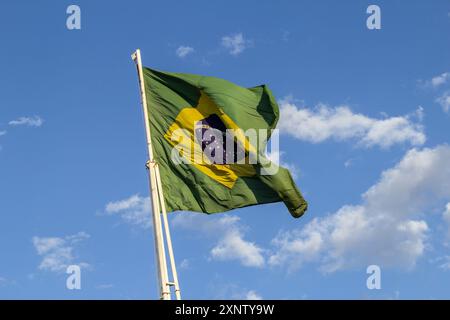 Goiania, Goias, Brasilien – 2. August 2024: Die brasilianische Flagge flattert auf dem Fahnenmast mit dem Himmel und einigen Wolken im Hintergrund. Stockfoto