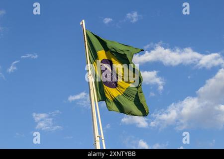 Goiania, Goias, Brasilien – 2. August 2024: Die brasilianische Flagge flattert auf dem Fahnenmast mit dem Himmel und einigen Wolken im Hintergrund. Stockfoto