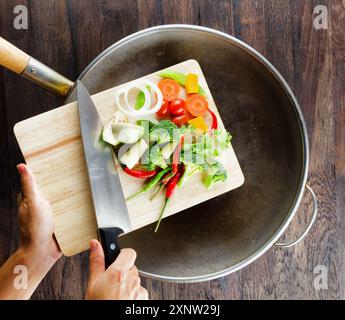 Frisches Gemüse auf dem Schneidebrett fällt in den Wok. Co Stockfoto