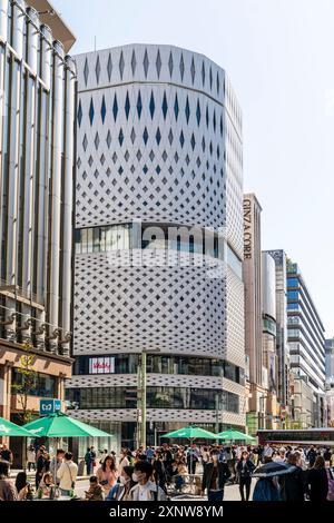 Der Ginza Place mit dem Ginza Core Gebäude daneben an einem sonnigen Wochenende mit Leuten, die die Fußgängerzone entlang laufen. Blauer Himmel. Stockfoto