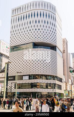 Der Ginza Place mit dem Ginza Core Gebäude daneben an einem sonnigen Wochenende mit Leuten, die die Fußgängerzone entlang laufen. Blauer Himmel. Stockfoto