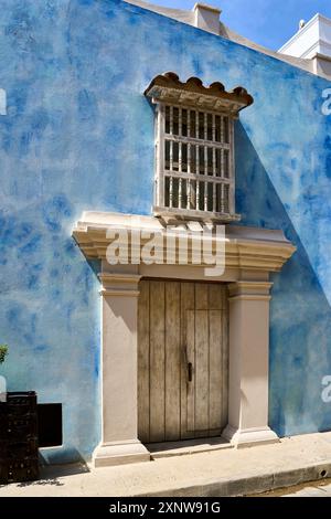 Alte Holztür und kunstvolles Fenster an einer blauen Wand in Cartagena, Kolumbien. Architektonische Details im Kolonialstil. Stockfoto