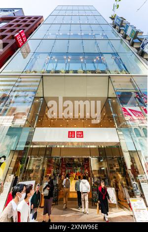 Flachwinkelansicht. Der Uniqlo-Laden auf der Ginza. Der Eingang ist voll mit Einkäufern, die ein- und ausgehen, und der Laden ragt dann über den Betrachter. Stockfoto