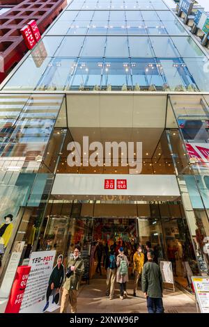 Flachwinkelansicht. Der Uniqlo-Laden auf der Ginza. Der Eingang ist voll mit Einkäufern, die ein- und ausgehen, und der Laden ragt dann über den Betrachter. Stockfoto