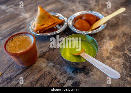 Eine Snackplatte mit Samosas, Chutney, süßem Gulab-Jamun und Kulhad Chai, die eine wunderschöne Mischung aus traditionellen Snacks und Kultur darstellt Stockfoto