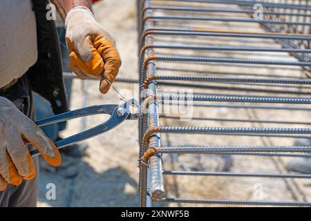 Ein Arbeiter verwendet Stahlbindungsseil, um Stahlstäbe an Verstärkungsstäben zu befestigen. Nahaufnahme. Die Stahlbetonkonstruktionen - das Stricken der metallischen Verstärkung Stockfoto