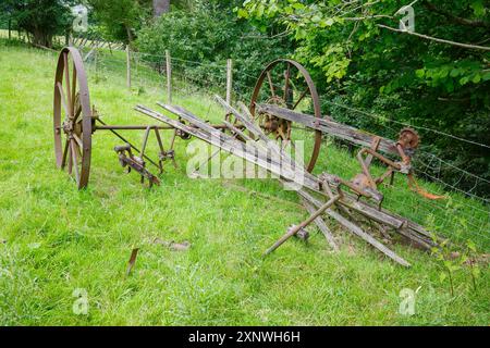 Rustikale Landwirtschaftsgeräte mit großen Metallrädern liegen an einem bewölkten Tag auf einem üppigen grünen Feld. Derbyshire UK. Stockfoto