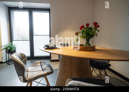 Esstisch mit Tellern, Gläsern und Vase mit roten Rosen. Innenausstattung einer modern eingerichteten Küche in einem neuen Haus. Esstisch und Stühle in stilvollem und Stockfoto