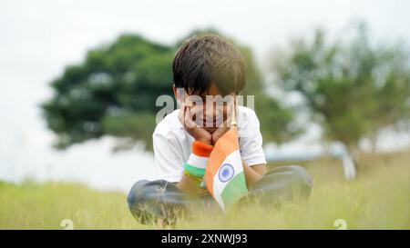 Glücklicher indischer, süßer, lächelnder kleiner Junge, der im Park eine dreifarbige Flagge schwenkt, um den Unabhängigkeitstag oder den Tag der Republik zu feiern. Stockfoto