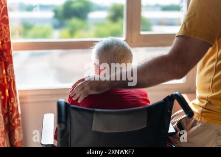 Ein junger Mann mit der Hand auf der Schulter einer älteren Frau mit weißem Haar, die im Rollstuhl sitzt. Stockfoto