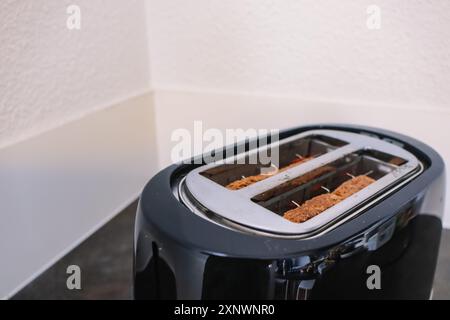Schwarzer Toaster in Betrieb mit zwei Brotscheiben in der Küche vor dem Hintergrund einer weißen Wand Stockfoto