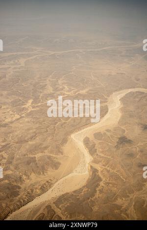 Dieses Luftbild zeigt ein trockenes Flussbett, das sich durch das karge und zerklüftete Gelände des Oman schlängelt. Die desolate Szene kann metaphorisch die Herausforderungen und Widerstandskraft darstellen, die in den Widrigkeiten zu finden sind. Stockfoto