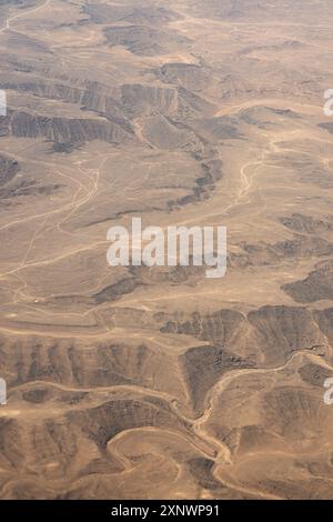 Blick aus der Vogelperspektive auf zerklüftetes, bergiges Gelände in Oman mit gewundenen Pfaden durch die trockene Landschaft. Die gewellten Formationen und Texturen erfassen die Essenz natürlicher Schönheit und Widerstandsfähigkeit. Stockfoto