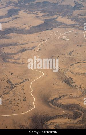 Ein Luftbild, das eine kurvenreiche Straße durch die trockene Wüstenlandschaft im Oman fotografiert. Dieses Bild repräsentiert metaphorisch die Reise des Lebens, der Widerstandsfähigkeit und der Ausdauer unter schwierigen Bedingungen. Stockfoto
