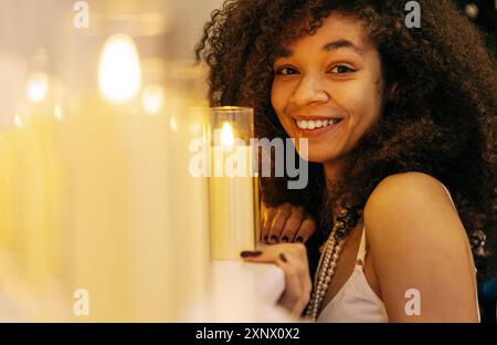 Eine Nahaufnahme einer jungen, lächelnden Afrikanerin zu Hause. Ein charmantes, lachendes schwarzes Mädchen in der Nähe von brennenden Kerzen. Ein attraktiver Teenager in einem eleganten fest Stockfoto